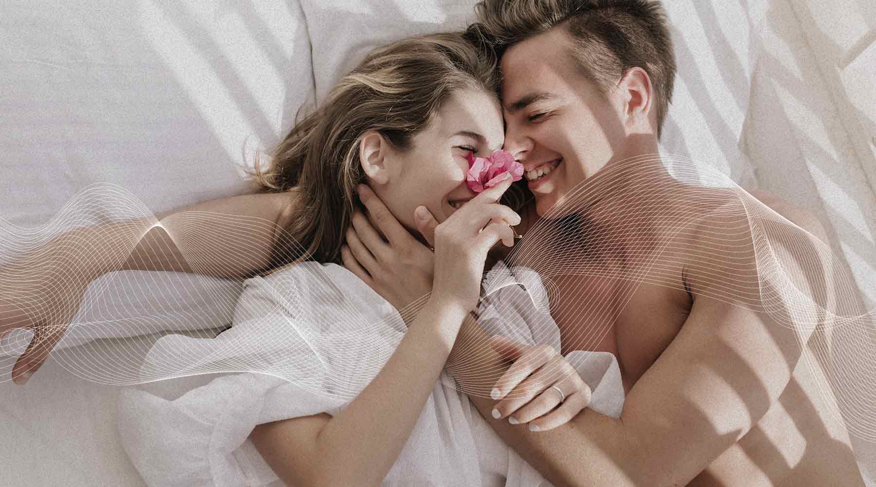 Pareja enamorada sonriendo tendidos en cama con flor rosada