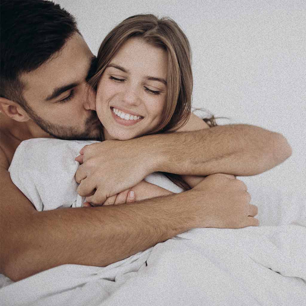 Pareja feliz y enamorada donde el hombre abraza tiernamente a la mujer por su espalda mientras ella le toma su mano.